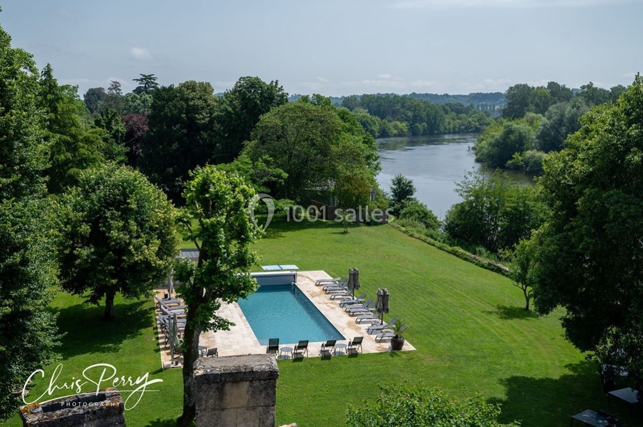 Vue d'un jardin verdoyant avec piscine, transats et arbres, surplombant une rivière entourée de végétation.