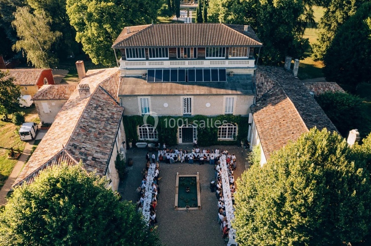 Vue aérienne d'un bâtiment ancien entouré de verdure, avec des tables dressées en extérieur pour un grand rassemblement.