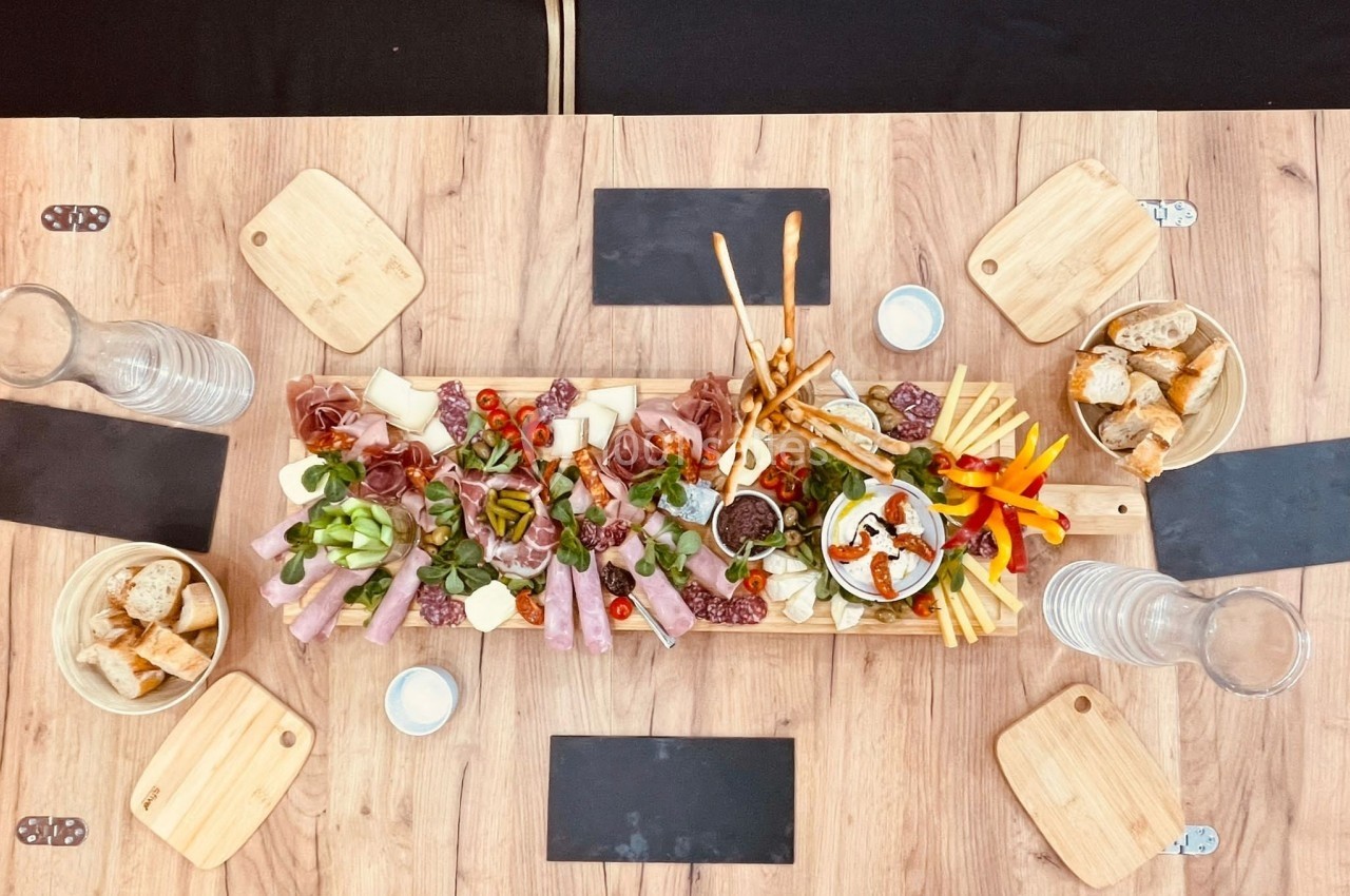 Plateau de charcuterie et fromages avec légumes, pains et sauces, disposé sur une table en bois.