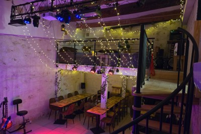 Miniature Location salle Antibes (Alpes-Maritimes) - La Fourmilière #2 Intérieur d'un bar chaleureux avec comptoir en bois, étagères à bouteilles, éclairage tamisé et décorations florales.