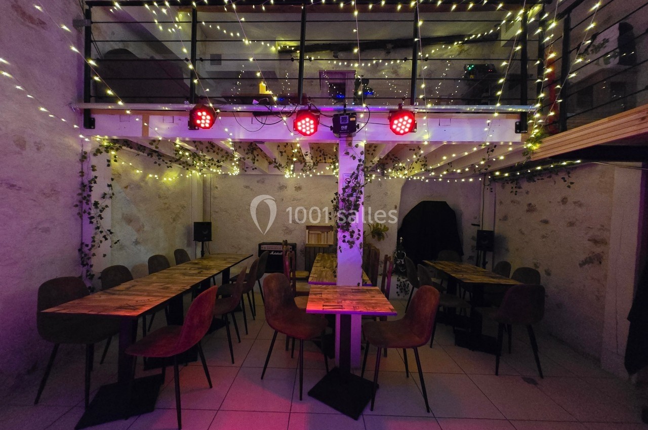 Salle décorée avec des guirlandes lumineuses, tables en bois et chaises, ambiance chaleureuse et éclairage tamisé.