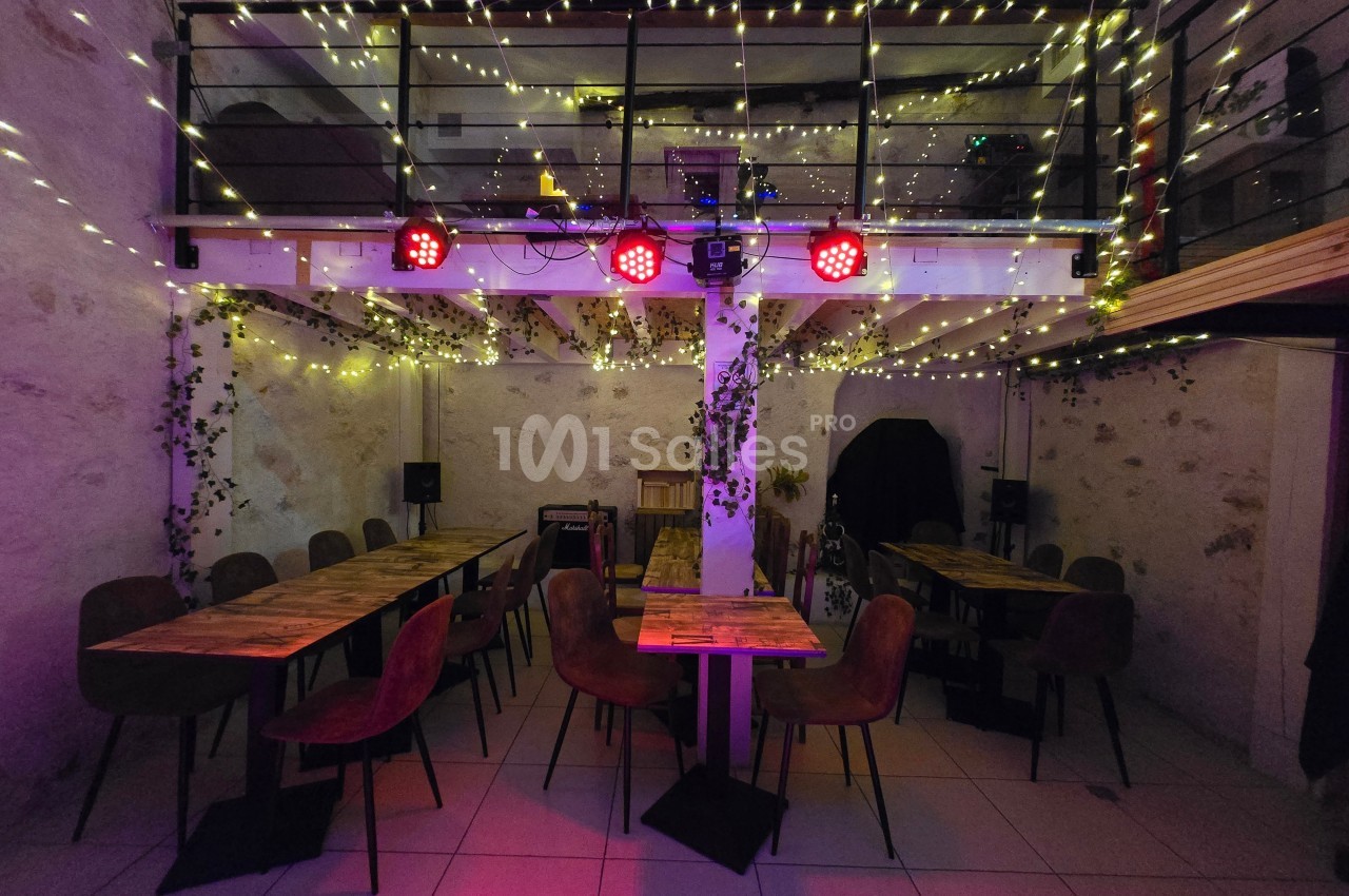 Salle décorée avec des guirlandes lumineuses, tables en bois et chaises, ambiance chaleureuse et éclairage tamisé.