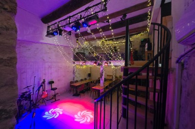 Miniature Location salle Antibes (Alpes-Maritimes) - La Fourmilière #7 Intérieur d'un bar chaleureux avec comptoir en bois, étagères à bouteilles, éclairage tamisé et décorations florales.