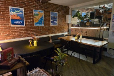 Miniature Location salle Antibes (Alpes-Maritimes) - La Fourmilière #8 Intérieur d'un bar chaleureux avec comptoir en bois, étagères à bouteilles, éclairage tamisé et décorations florales.