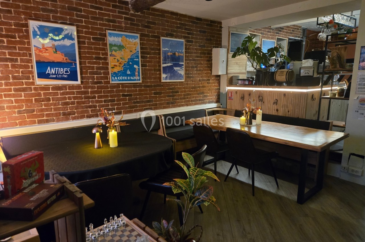 Salle de restaurant chaleureuse avec murs en briques, tables en bois, affiches rétro et éclairage tamisé.