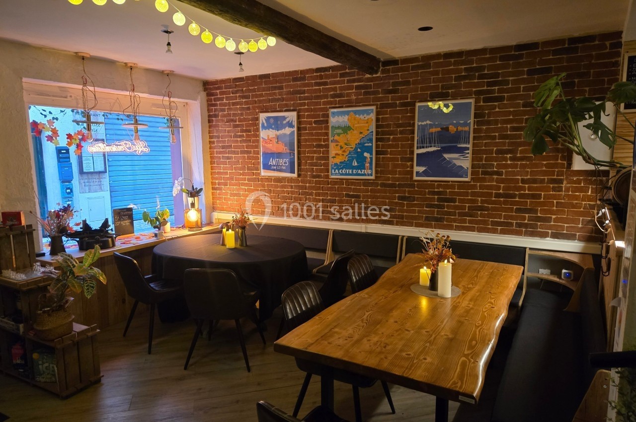 Salle à manger chaleureuse avec murs en briques, tables en bois, chaises noires et décoration lumineuse.