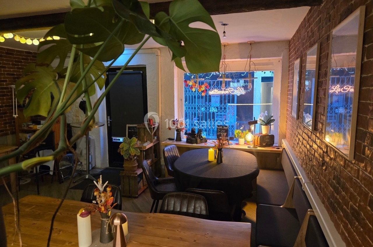 Salle à manger chaleureuse avec table en bois, chaises noires, plantes et éclairage tamisé près d'une fenêtre.