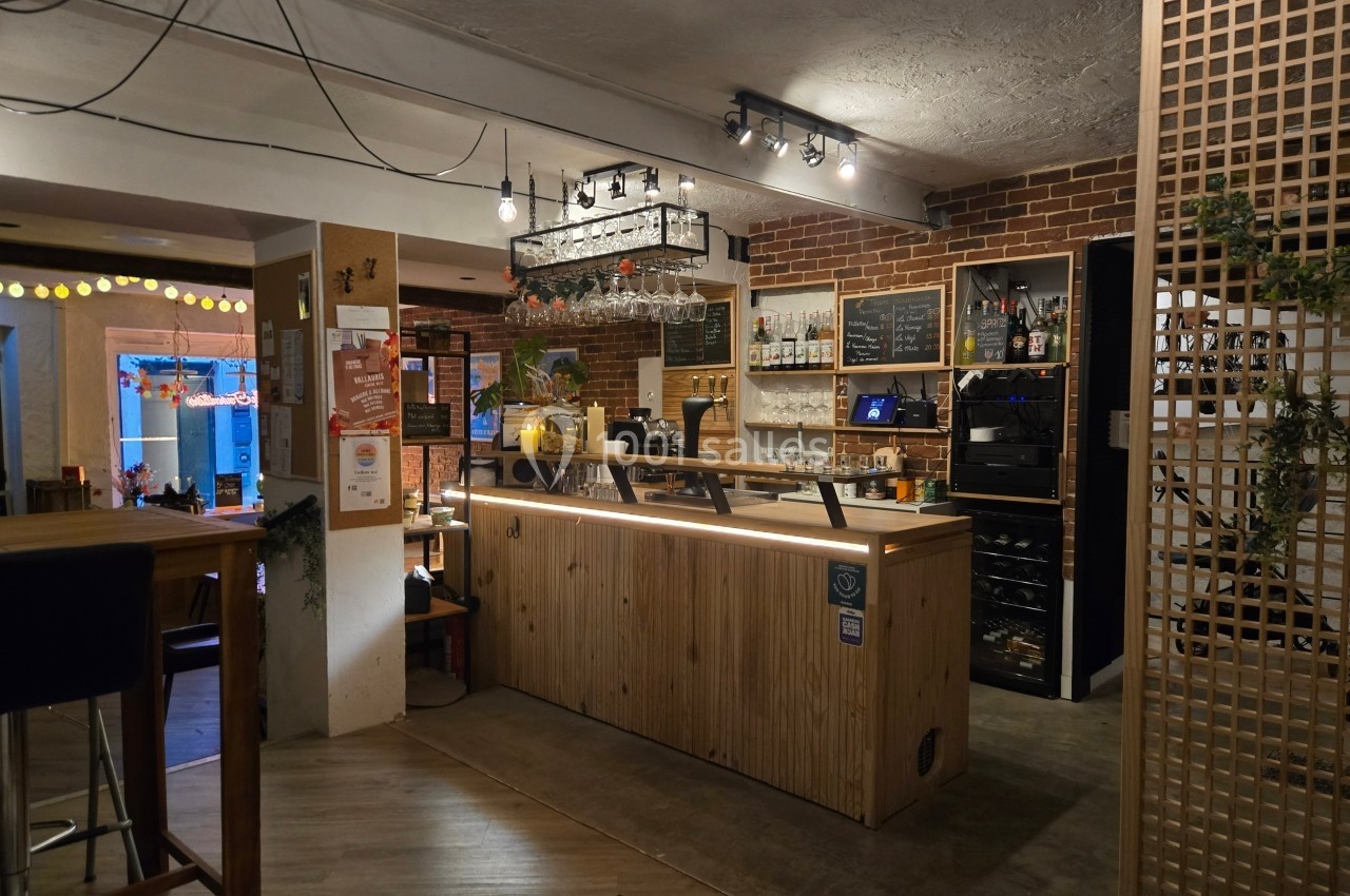 Intérieur d'un café moderne avec un comptoir en bois, des étagères garnies de bouteilles et un éclairage chaleureux.
