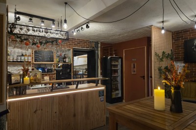 Miniature Location salle Antibes (Alpes-Maritimes) - La Fourmilière #11 Intérieur d'un bar chaleureux avec comptoir en bois, étagères à bouteilles, éclairage tamisé et décorations florales.