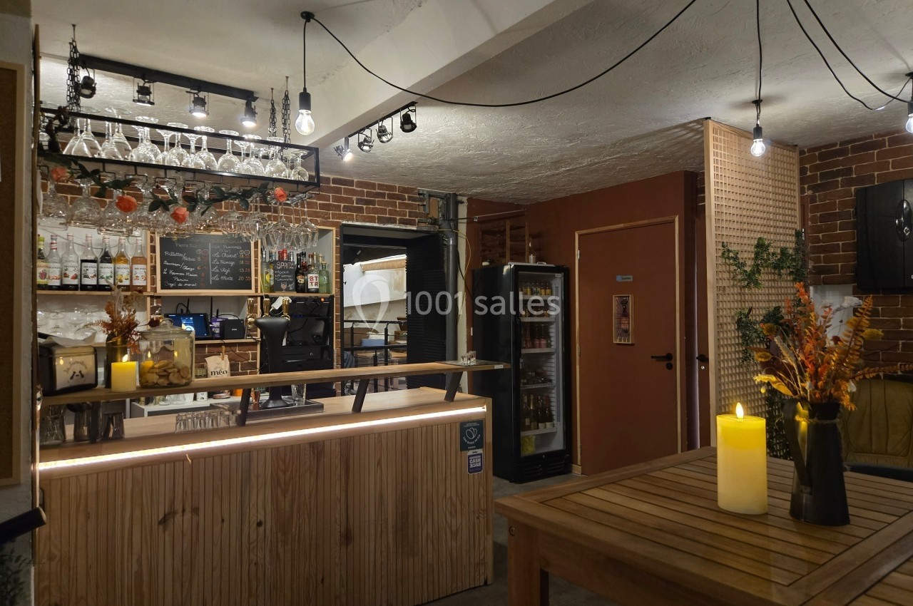 Intérieur d'un bar chaleureux avec comptoir en bois, étagères à bouteilles, éclairage tamisé et décorations florales.