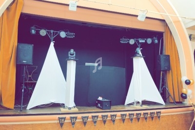 Scène décorée avec des rideaux orange, des enceintes, des lumières et une table de DJ pour un événement festif.