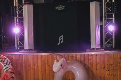 Un DJ mixe sur une scène éclairée avec des jeux de lumière, un bouée licorne posée devant.