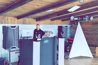 Un DJ anime un espace couvert avec des équipements audio et un éclairage installé sur une scène en bois.