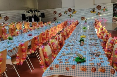 Salle décorée pour un événement, avec longues tables recouvertes de nappes à carreaux et chaises ornées de guirlandes…