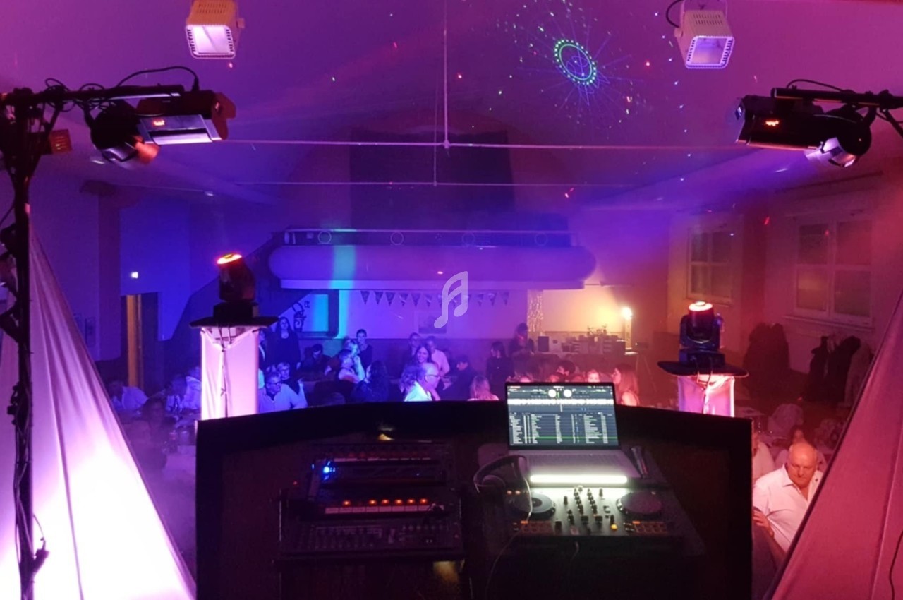 Vue depuis une cabine de DJ avec éclairages colorés et invités assis dans une salle de réception.