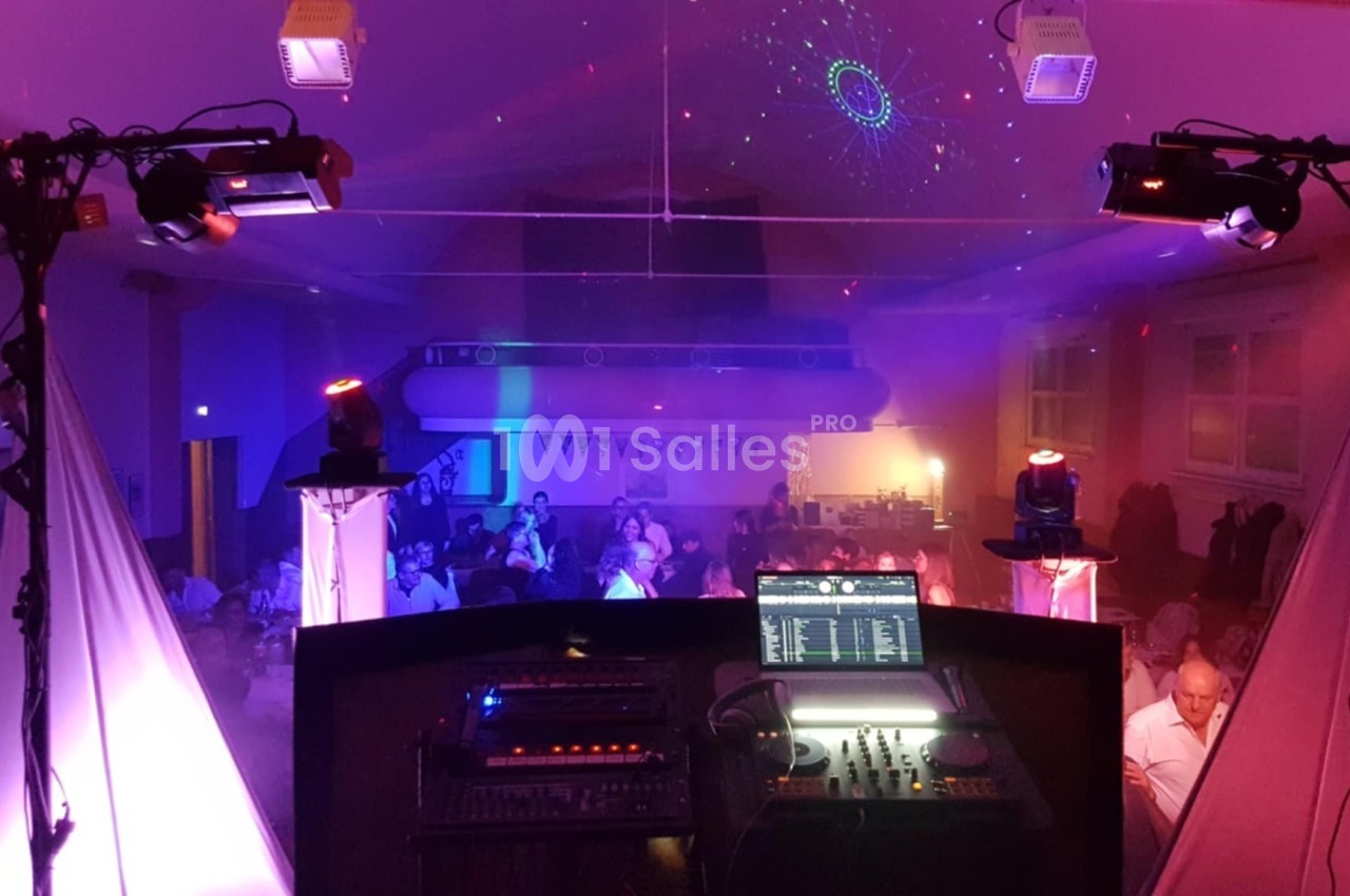 Vue depuis une cabine de DJ avec éclairages colorés et invités assis dans une salle de réception.