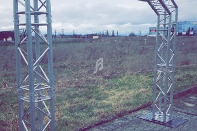 Structure métallique en forme d'arche installée sur un sol pavé, avec un paysage extérieur en arrière-plan.