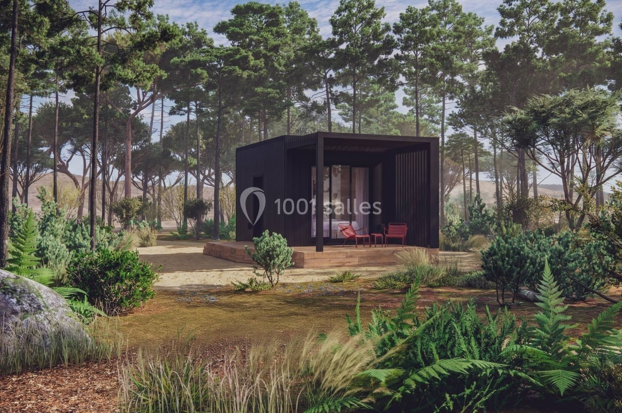 Cabane moderne en bois sombre entourée de végétation dense et de pins dans un environnement naturel.