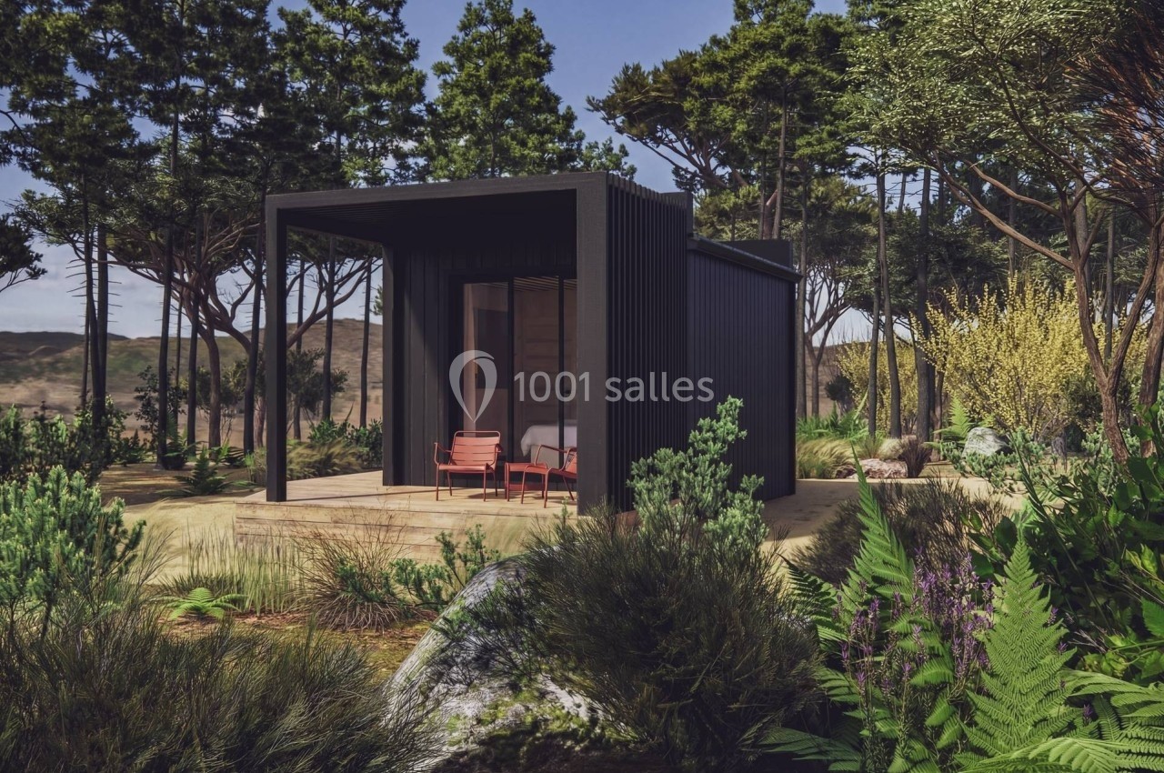 Petite maison moderne noire entourée de végétation dense et d'arbres dans un environnement naturel.