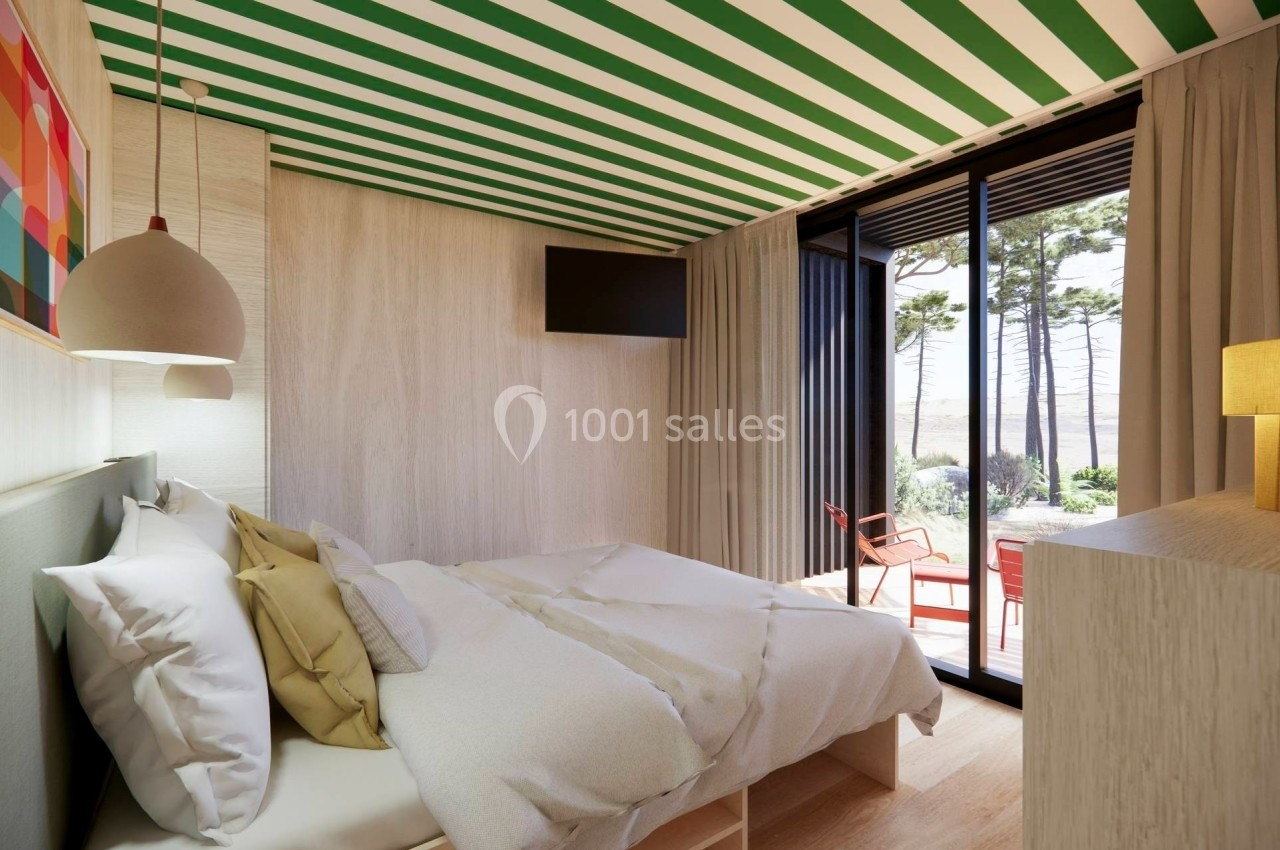 Chambre lumineuse avec lit double, décor moderne, plafond rayé vert et blanc, et vue sur une terrasse extérieure arborée.