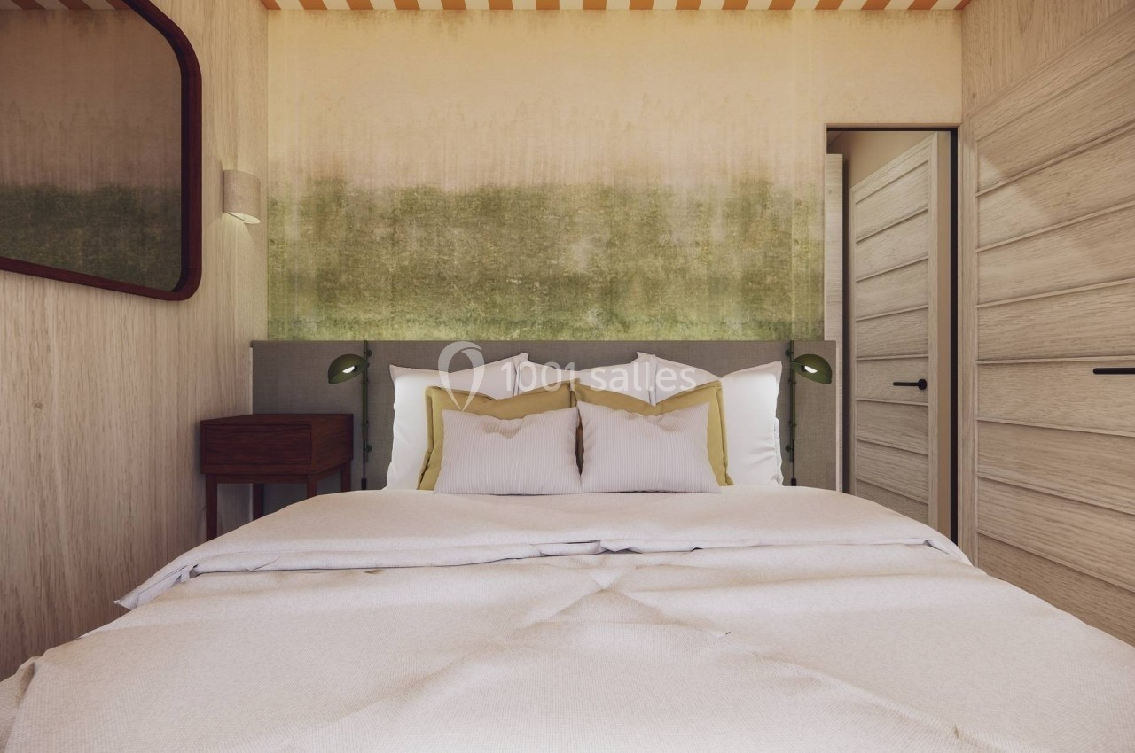 Lit double avec draps blancs, coussins jaunes, table de chevet en bois et mur texturé dans une chambre lumineuse.