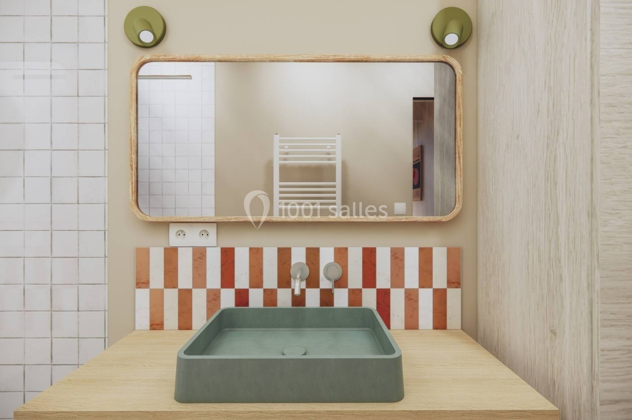 Lavabo vert sur un plan en bois, miroir rectangulaire encadré, carreaux rouges et blancs en arrière-plan.