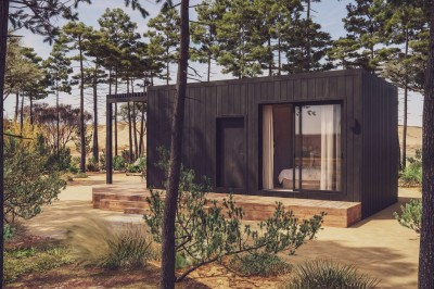 Vue aérienne d'une petite maison avec terrasse en bois, salon, chambre, salle de bain et environnement naturel autour.