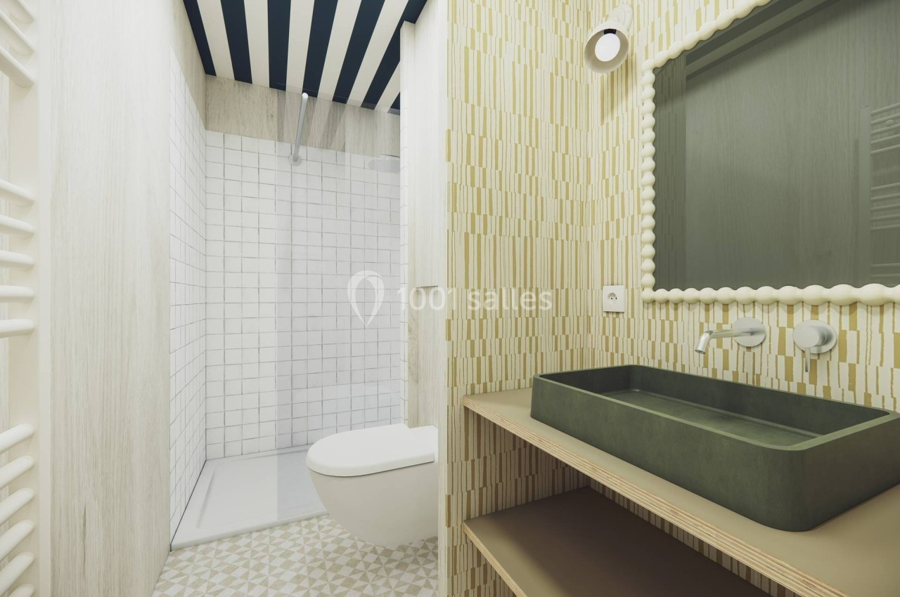Salle de bain moderne avec douche à l'italienne, lavabo vert, miroir encadré et carrelage géométrique beige.
