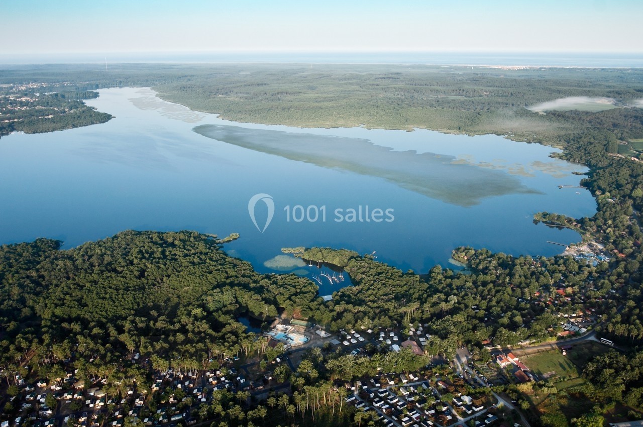 Vue aérienne d'un grand lac entouré de forêts, avec des habitations et un camping visible au premier plan.