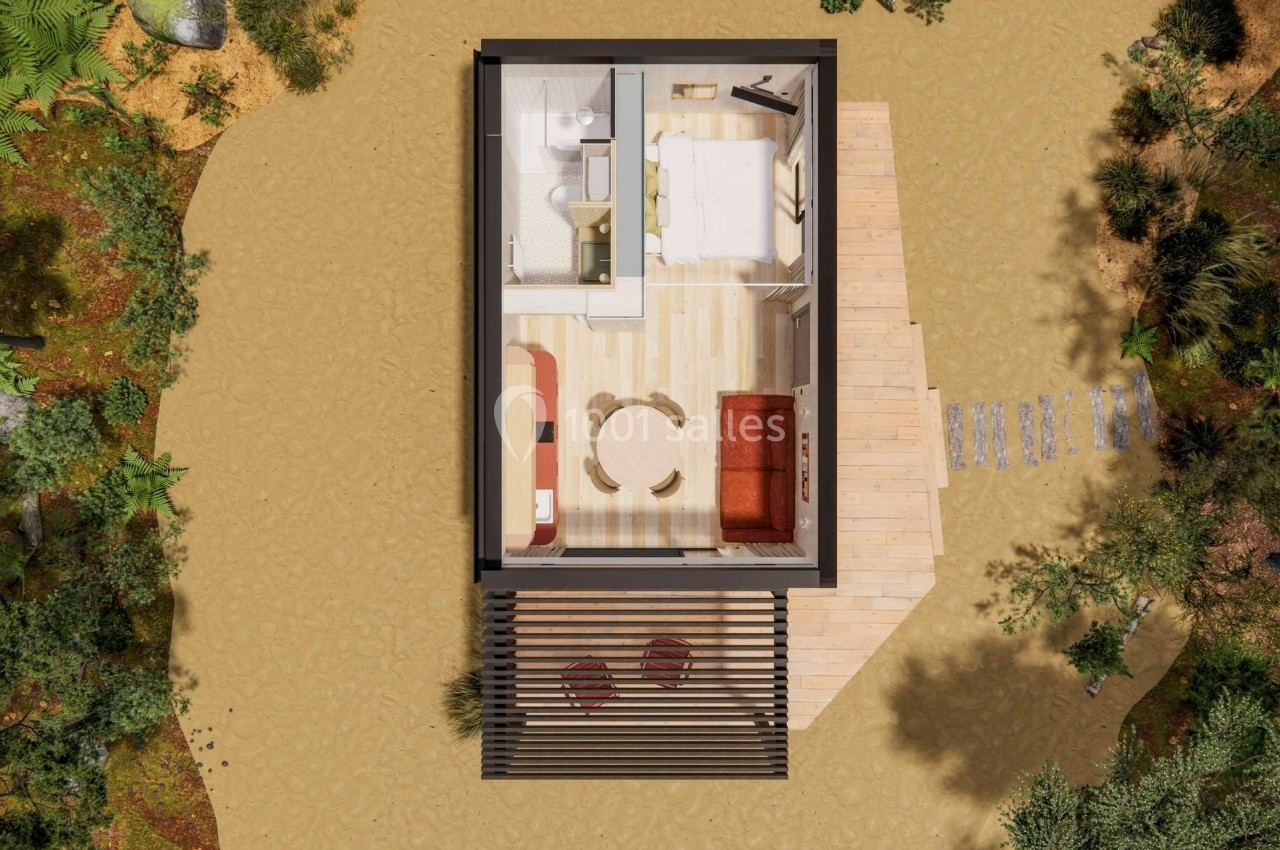 Vue aérienne d'une petite maison avec terrasse en bois, salon, chambre, salle de bain et environnement naturel autour.