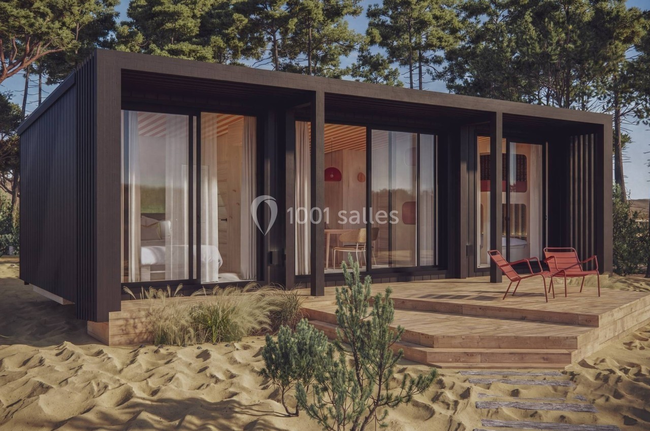 Maison préfabriquée moderne avec façade en bois sombre, grande baie vitrée et terrasse aménagée dans un environnement boisé.