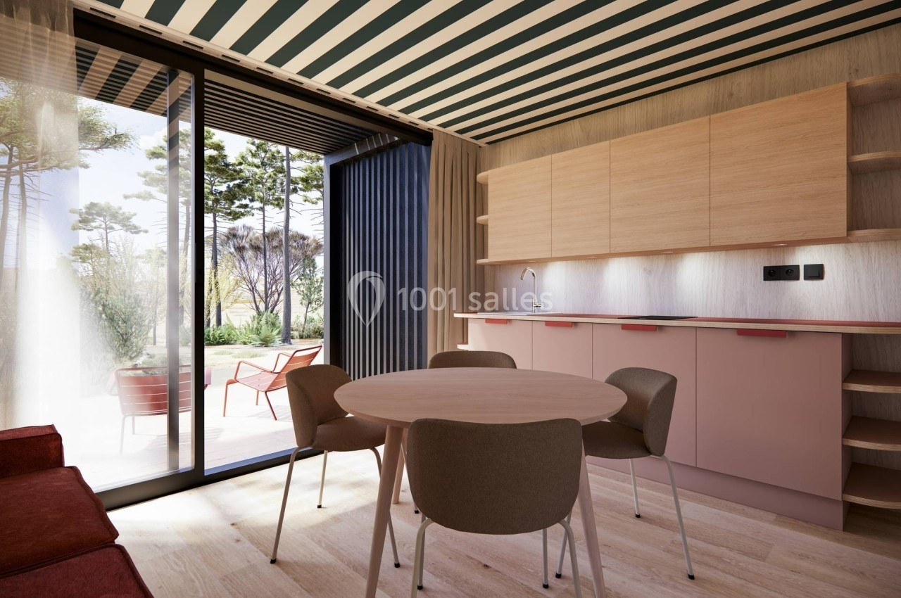 Intérieur lumineux avec table ronde, chaises, cuisine en bois clair et vue sur une terrasse donnant sur un jardin.