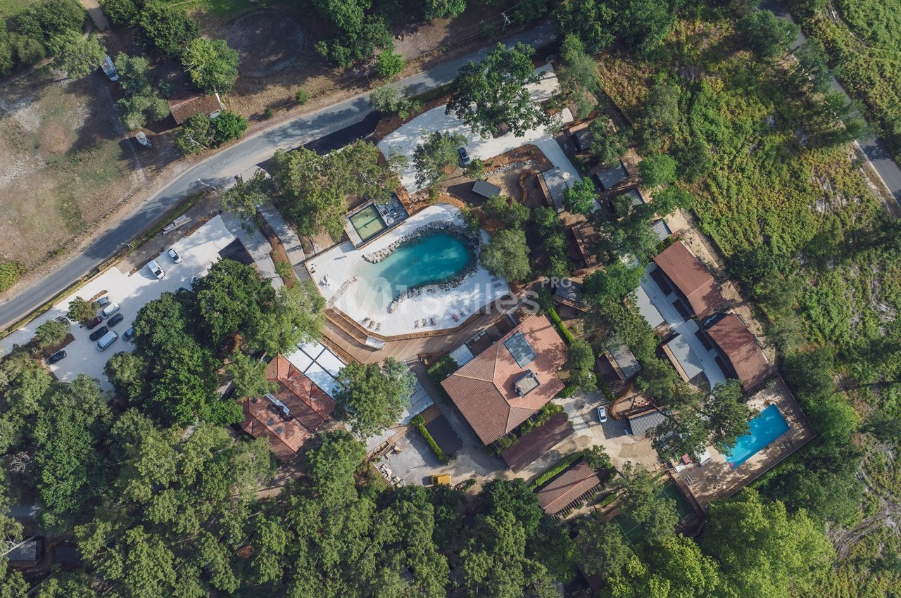 Vue aérienne d'un complexe avec piscine, bâtiments et espaces verts entourés de végétation dense.