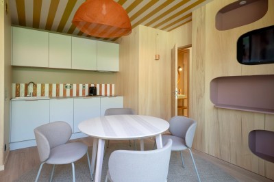 Miniature Hébergement - MINI VILLA Intérieur d'un petit appartement moderne avec salon, table à manger, cuisine et lit visible en arrière-plan.