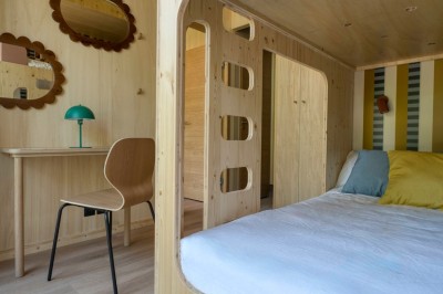 Miniature Hébergement - MINI VILLA Intérieur d'un petit appartement moderne avec salon, table à manger, cuisine et lit visible en arrière-plan.