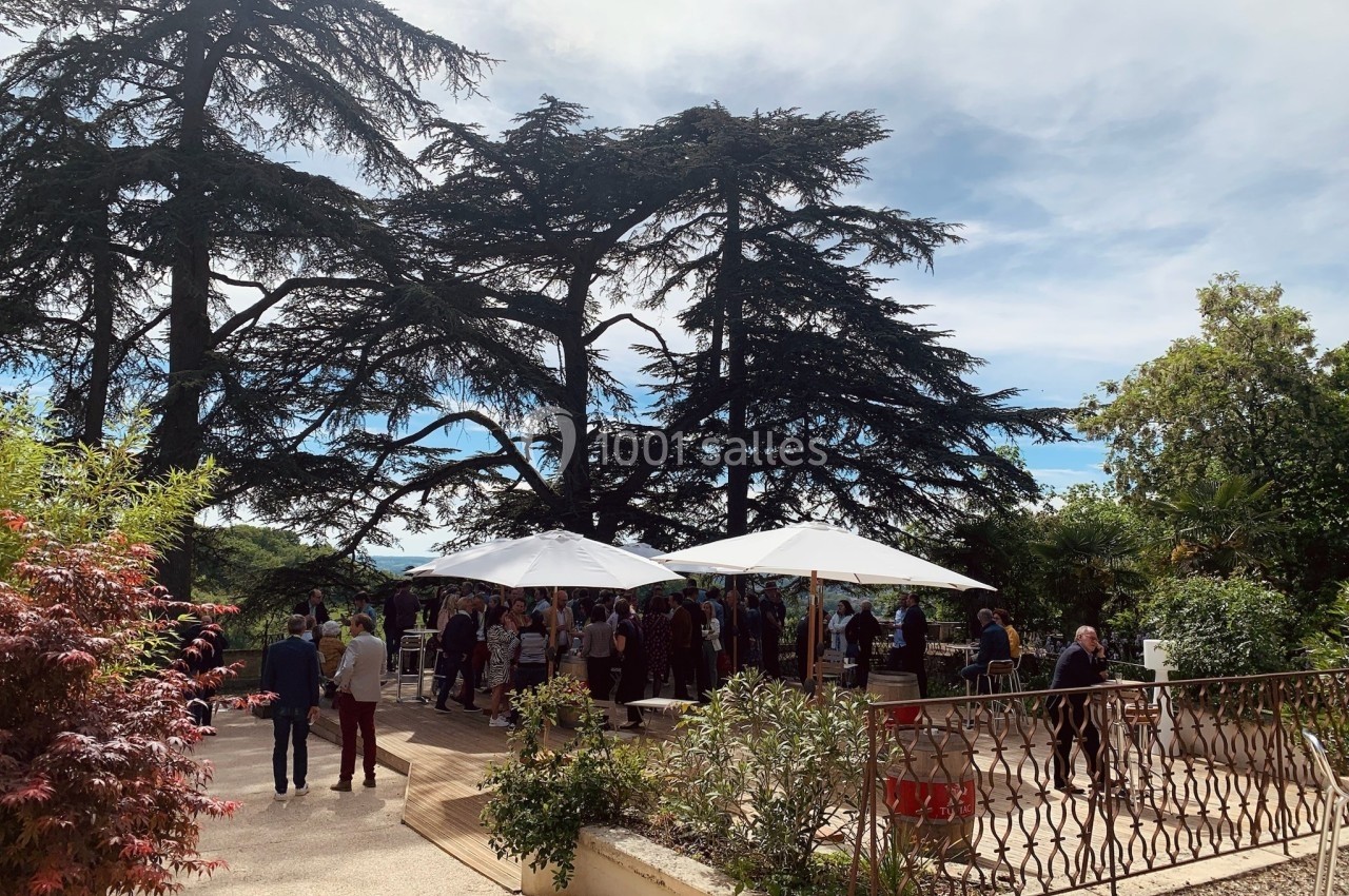 Groupe de personnes réunies sous des parasols dans un jardin arboré par une journée ensoleillée.