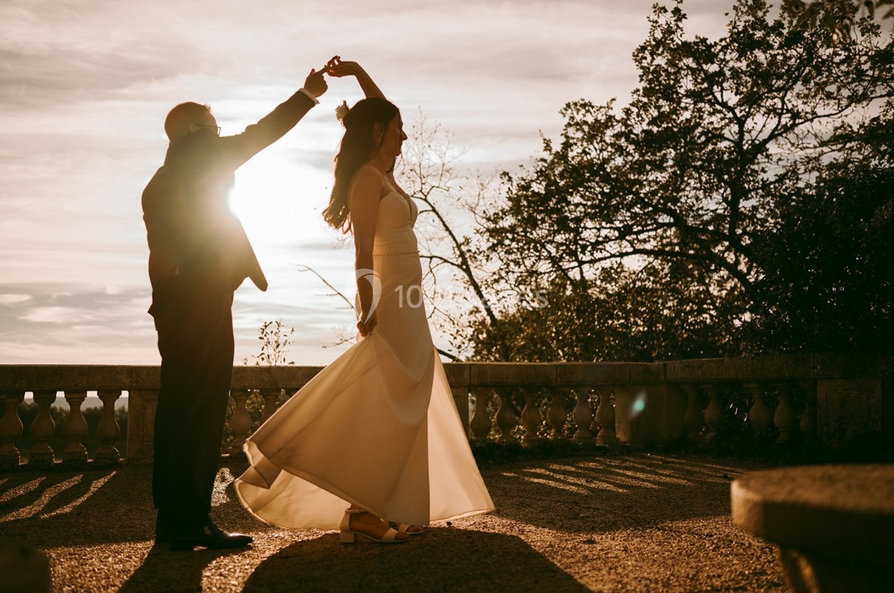Un couple danse en plein air au coucher du soleil, entouré de balustrades et d'arbres.