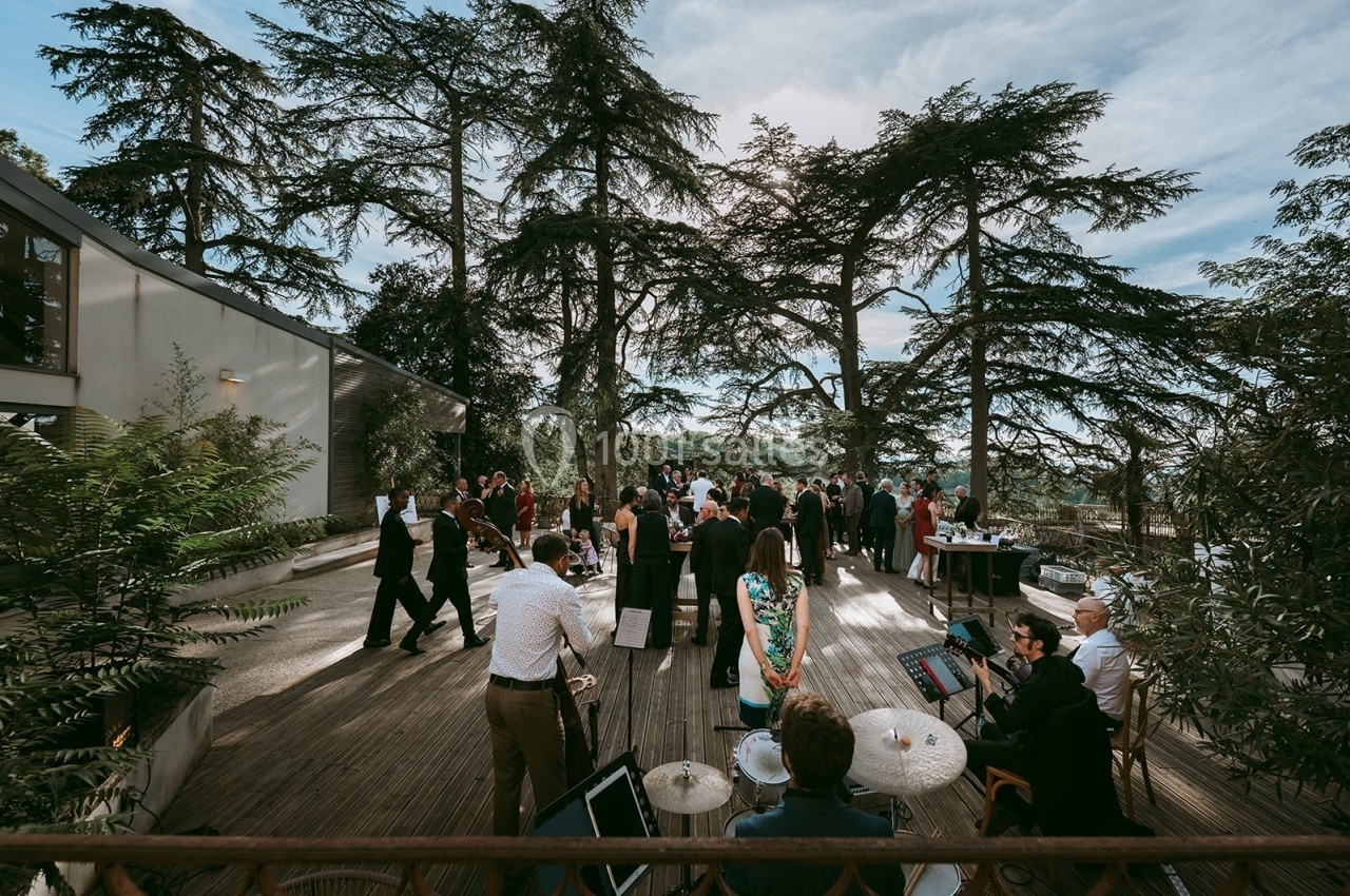 Groupe de personnes rassemblées sur une terrasse en bois entourée d'arbres, lors d'un événement en plein air.