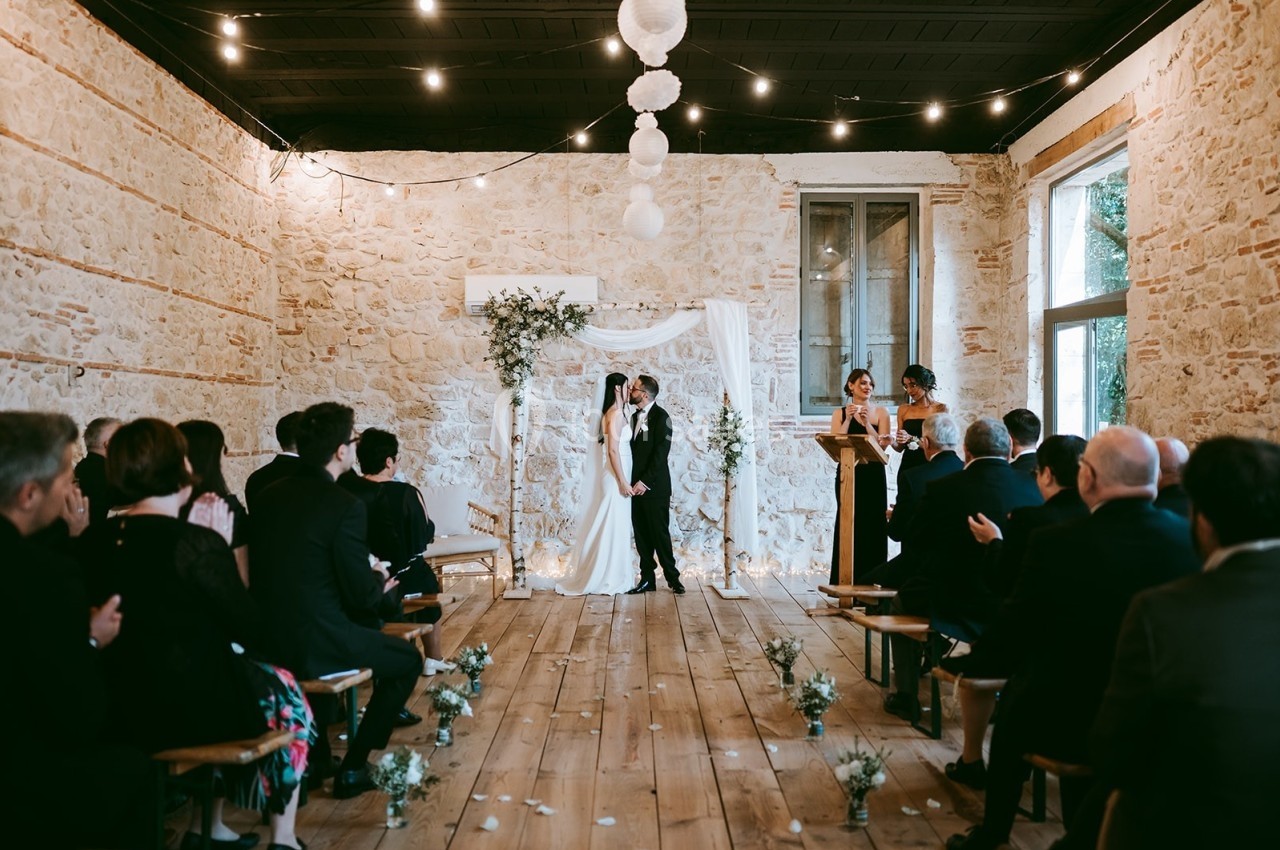 Cérémonie de mariage dans une salle en pierre, avec les mariés devant un autel décoré et des invités assis.