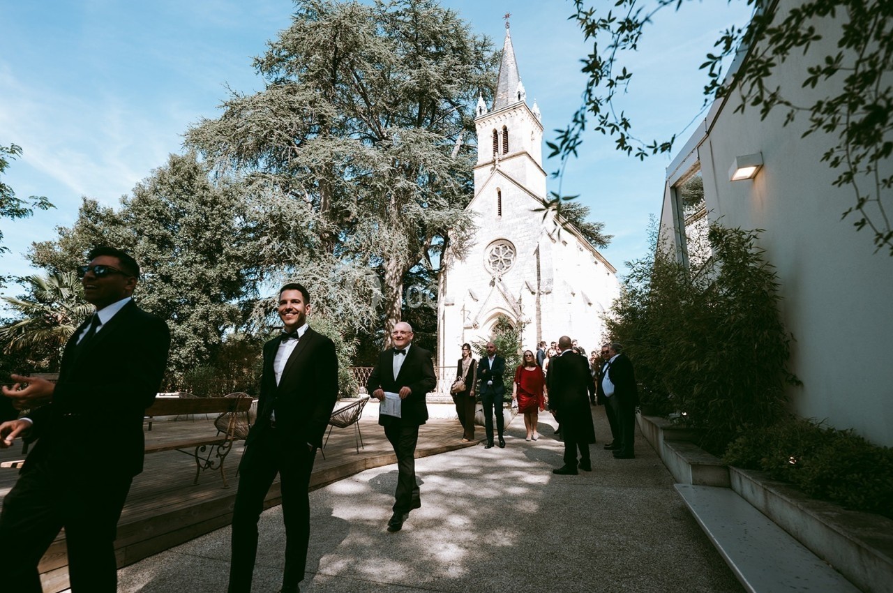 Des personnes en tenue élégante marchent près d'une église entourée d'arbres par une journée ensoleillée.
