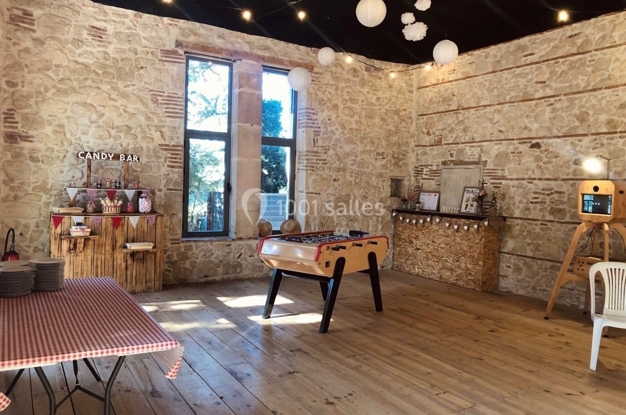 Salle en pierre avec baby-foot, candy bar, guirlandes lumineuses et décorations suspendues.