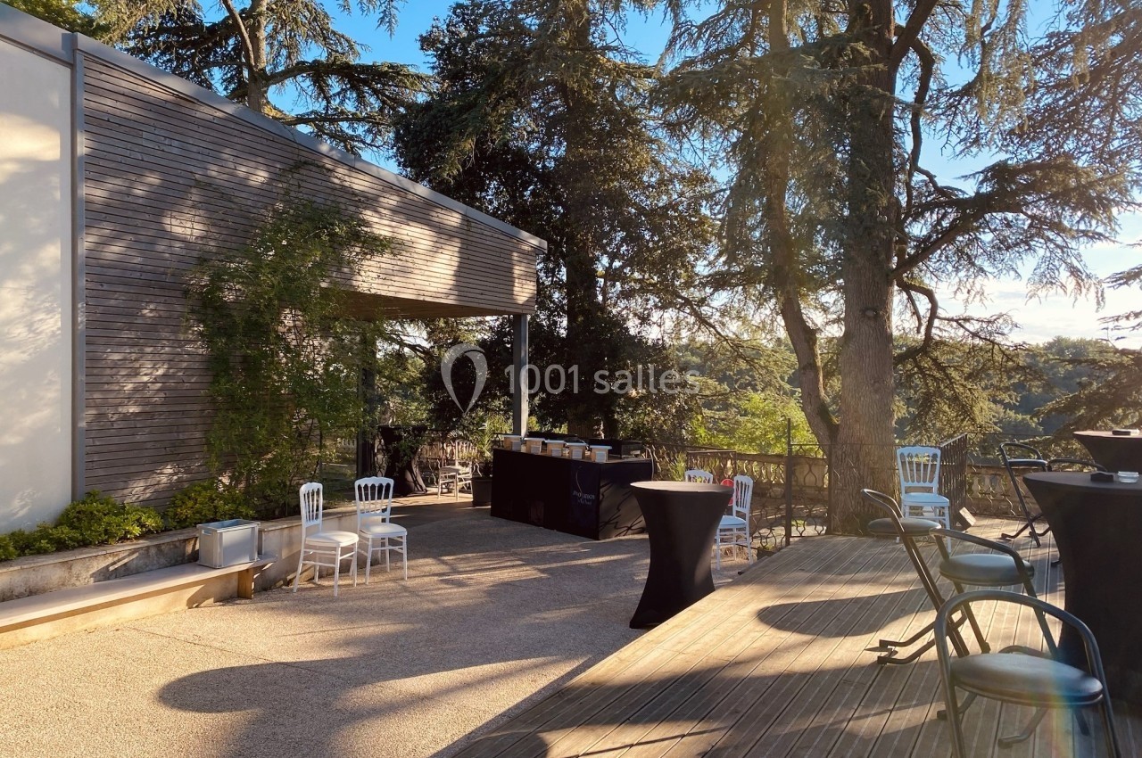 Terrasse ensoleillée avec mobilier d'extérieur, entourée d'arbres et d'un bâtiment en bois moderne.