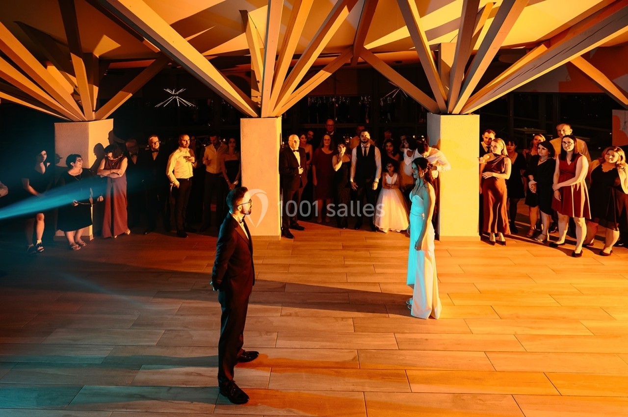 Un couple en tenue de mariage se fait face sur une piste de danse, entouré d'invités sous une structure lumineuse.