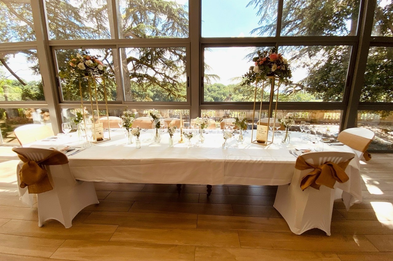 Table de réception élégamment dressée avec nappes blanches, décorations florales et grandes baies vitrées donnant sur un…