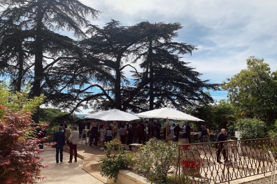 Salle en pierre avec parquet, tables dressées pour un repas, grandes fenêtres et éclairage suspendu.