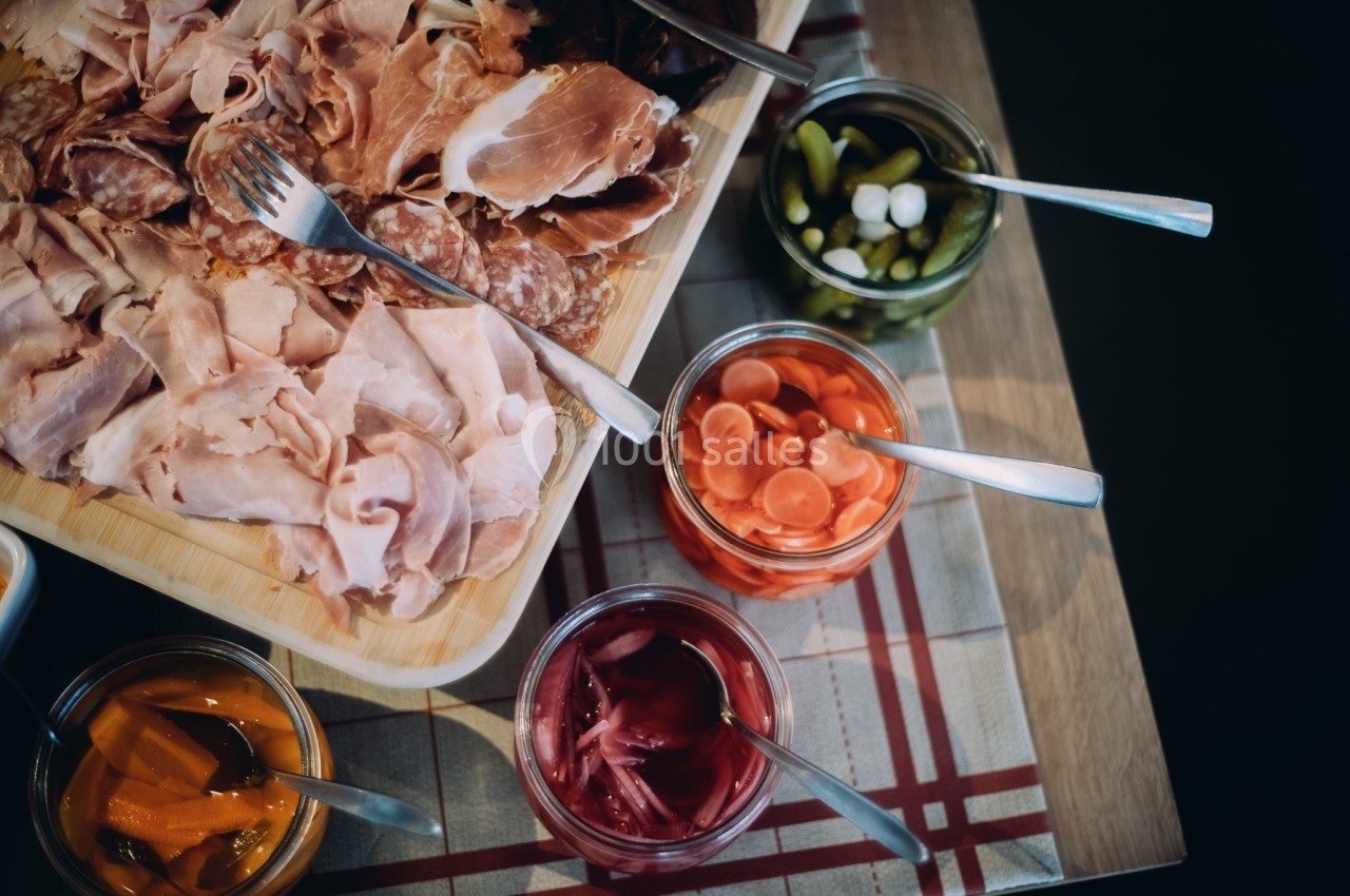 Plateau de charcuterie accompagné de bocaux de légumes marinés, disposés sur une nappe à carreaux.