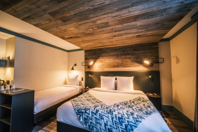 Chambre d'hôtel moderne avec lit double, décor en bois, salle de bain ouverte et vue sur l'extérieur par une baie vitrée.