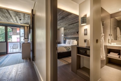 Chambre d'hôtel moderne avec lit double, décor en bois, salle de bain ouverte et vue sur l'extérieur par une baie vitrée.