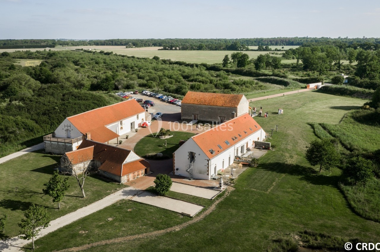 Vue aérienne d'un ensemble de bâtiments à toits rouges entourés de verdure et de chemins dans une zone rurale.