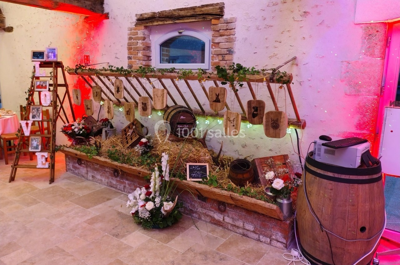 Décoration rustique avec tonneaux, fleurs, guirlandes et lettres suspendues dans une salle aux murs en pierre.